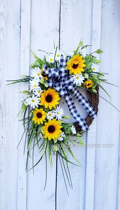 a wreath with sunflowers and daisies hanging on a white fence