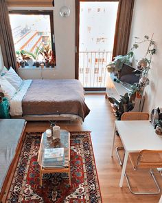 a living room with a bed, table and chairs in it next to a window