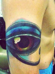 an eye tattoo on the back of a man's left arm, with blue and green colors