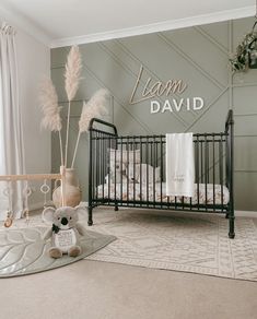 a baby's room with a crib, teddy bear and name sign on the wall