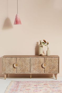 a wooden cabinet with two vases on top and a rug in the corner next to it