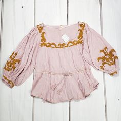 Gorgeous Bohemian Festival Top From Free People. Features A Flattering Square Neckline, Gorgeous 3/4 Lenght Puff Sleeves Finished With An Embroidered Button Cuff, Tie Waist With Tassel Rope And Lush Gold Embroidery Detailing. A Chic And Comfortable Cotton/Rayon Blend. Hand Wash. Color Is Pink/Rose, A Light Lavender-Pink Color With Lush Gold Embroidery. New With Tags. Size Medium. Measurements Taken Flat And Are Approximate: Bust 18", Adjustable Waist Up To 20", Length 23", Sleeve 19". Fitted Pink Bohemian Blouse, Spring Pink Cotton Blouse, Fitted Pink Embroidered Tops, Fitted Embroidered Pink Tops, Pink Cotton Blouse For Spring, Feminine Pink Embroidered Top For Summer, Feminine Pink Embroidered Summer Top, Pink Peasant Top For Summer, Pink Bohemian Top