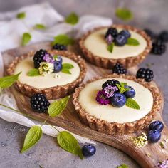 three small pies with fresh berries and mint sprigs on top are sitting on a wooden cutting board