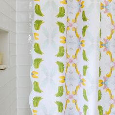 a shower curtain with green and yellow leaves on it in a white tiled bathroom area