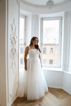 a woman standing in front of a window wearing a white dress