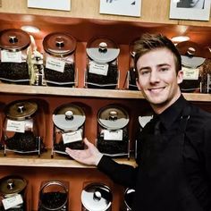 a man standing in front of a shelf filled with coffee beans and other things on it