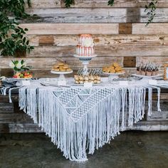 a table topped with cakes and cupcakes covered in icing next to a wooden wall