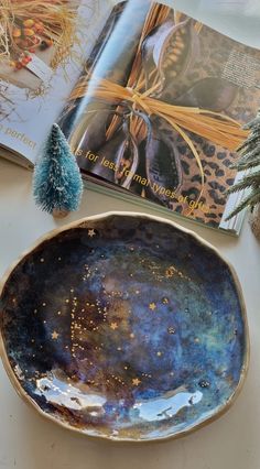 an open book on a table next to a blue bowl with gold speckles