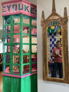 a woman standing in front of a mirror next to a replica of a phone booth