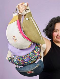 a woman is holding several purses in her hands and smiling at the camera while standing against a purple background