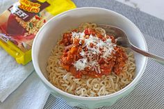 a bowl of pasta with meat sauce and parmesan cheese on top next to a bag of chips