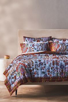 the bed is made up with colorful pillows and blankets on it, along with an end table