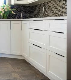 a kitchen with white cabinets and black counter tops is pictured in this image, there are flowers on the counter