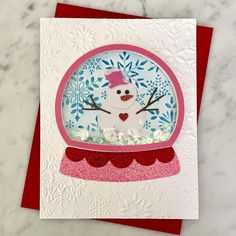 a card with a snowman in a glass ball on it's side and red envelope