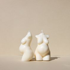 two white candles sitting next to each other on top of a table with a beige wall in the background