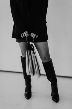 a woman with long hair and boots is holding a bag in her hand while standing on the floor