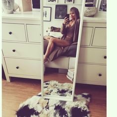 a woman sitting in front of a mirror on top of a floor next to a dresser