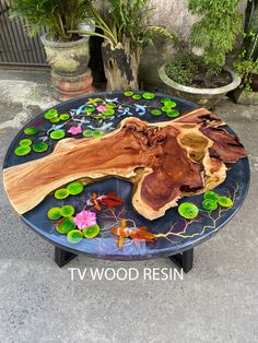 a table made out of wood with flowers and leaves on it, sitting in front of a potted plant