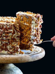 a person is holding a fork and cutting into a carrot cake with pecans on top