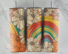 three colorful floral tumbles hanging on a marble wall with a rainbow in the background