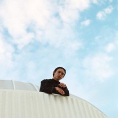 a man standing on top of a white building with his arms crossed and looking off into the distance