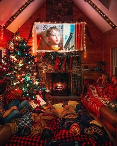 two people sitting on couches in front of a christmas tree with lights and a flat screen tv