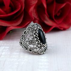 This stunning cocktail ring features an intricate filigree lace design and a 7x14 mm black onyx gemstone. Black onyx is a stone of protection and grounding, making it the perfect choice for a statement cocktail ring. It is said to absorb negative energy and promote inner strength.  Ring Face Length is 0.65 inches and Width is 0.30 inches  The ring is made from high-quality 925 sterling silver and is finished to a high shine. The lace detailing is exquisitely crafted and adds a touch of elegance to the ring. The ring comes with a silver polish cloth and a luxurious gift box, making it the perfect gift for any special occasion. This statement piece is perfect for any occasion, from a night out on the town to a special event. It is sure to turn heads wherever you go. Whether you are looking f Ornate Black Wedding Ring, Black Filigree Ring With Intricate Design For Formal Occasions, Elegant Black Jewelry With Intricate Design, Black Ring With Intricate Design, Black Oval Filigree Jewelry, Oval Black Filigree Jewelry, Black Oval Filigree Ring For Formal Occasions, Black Filigree Ring, Ornate Black Jewelry With Intricate Design