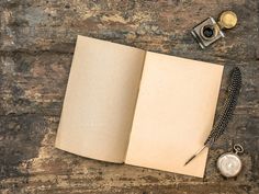 an open book with a pen, watch and other items on it next to a pocket watch