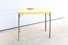 an old yellow table sitting in front of a garage door with a brown spot on it