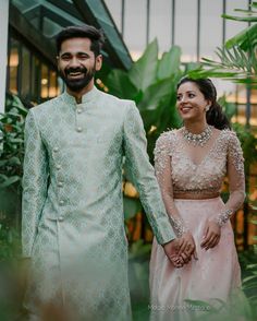 a man and woman holding hands while standing next to each other in front of plants