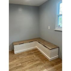 an empty room with a bench and window in the corner on the far wall is a hardwood floor