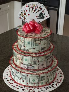 a cake made out of dollar bills and playing cards on top of it with a red bow