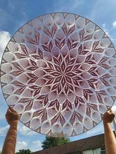 two hands holding up a large circular metal object in front of a blue sky with white clouds