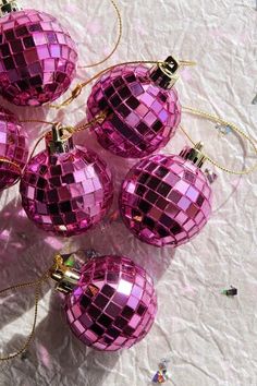 six pink disco ball ornaments sitting on top of a white tablecloth covered table with confetti sprinkles