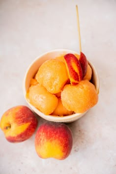 three peaches in a white bowl with two peaches on the table next to them