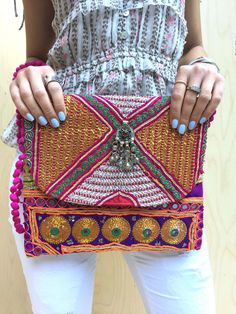 Our new bold embellished clutches come in new statement square shape and are beautiful handmade by local artisans of the Banjara tribe in India. Embellished with bold metallic thread these bags are a stunning accessory to any outfit. All bags are hand-crafted using patchworks of vintage Banjara embroidery and embellishments. According to some authorities, the Banjara lineage goes back some 2000 years. Wear as an over-sized clutch or on your shoulder with the light-weight cotton pompom chain.  Be Rectangular Clutch With Multicolor Embroidery For Festivals, Multicolor Embroidered Rectangular Clutch For Festivals, Rectangular Multicolor Embroidered Clutch For Festivals, Multicolor Embroidered Festival Clutch, Festival Multicolor Embroidery Handwork Clutch, Traditional Rectangular Clutch For Festivals, Multicolor Rectangular Clutch With Handwork, Rectangular Multicolor Clutch With Handwork, Festival Rectangular Clutch With Handwork