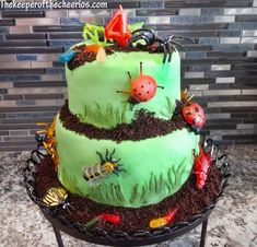 there is a green cake decorated with bugs and ladybugs on the top tier