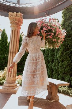 a woman in a white dress standing under a gazebo with pink flowers on it