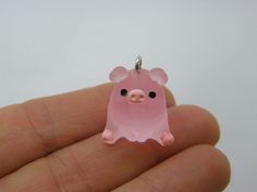 a tiny pink pig charm sitting on top of a person's finger in front of a white background