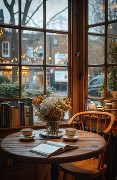 a wooden table with two cups and saucers on it in front of large windows