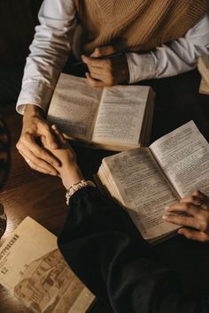 two people sitting at a table with open books in front of them, one holding the other's hand