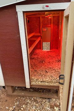 the inside of a barn with red light coming in from the door and hay on the floor