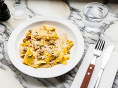 a white plate topped with pasta and sauce next to silverware on a marble table