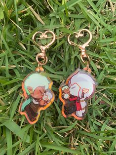 two key chains with anime characters on them laying in the grass, next to each other