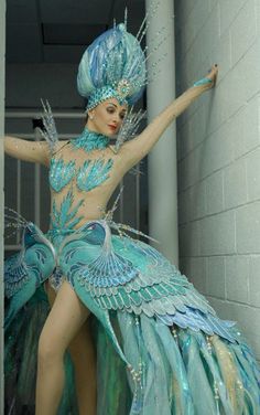 a woman in a blue dress and headdress is standing next to a wall