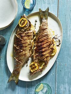 two fish are on a plate with lemons and spices next to it, along with other dishes