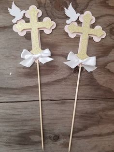 two cupcake toppers with bows and a cross on them, one is blue and the other is gold