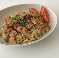 a white bowl filled with rice and meat next to a cherry tomato on the side