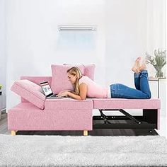 a woman laying on top of a pink couch next to a white table with a laptop