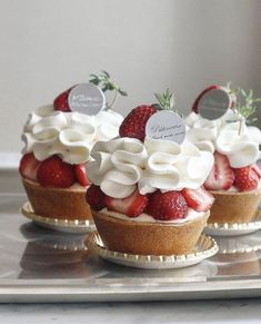 three small desserts with strawberries and whipped cream on top are sitting on a silver tray